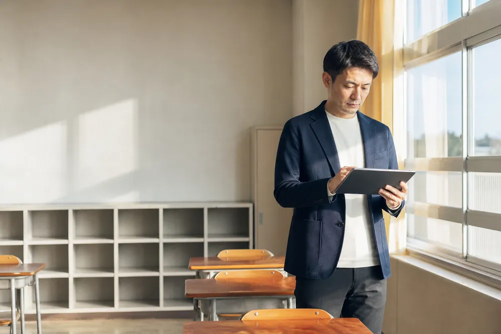 授業前の教室で一人、タブレットを手に準備をする先生（イメージ）